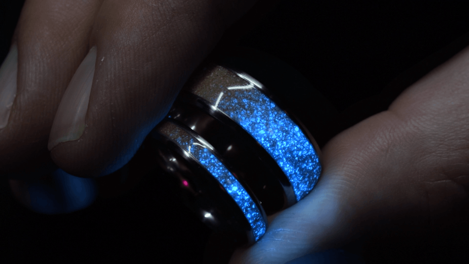 Sangreal Rings custom titanium sand ring with glowing blue sand inlay held between fingers close up