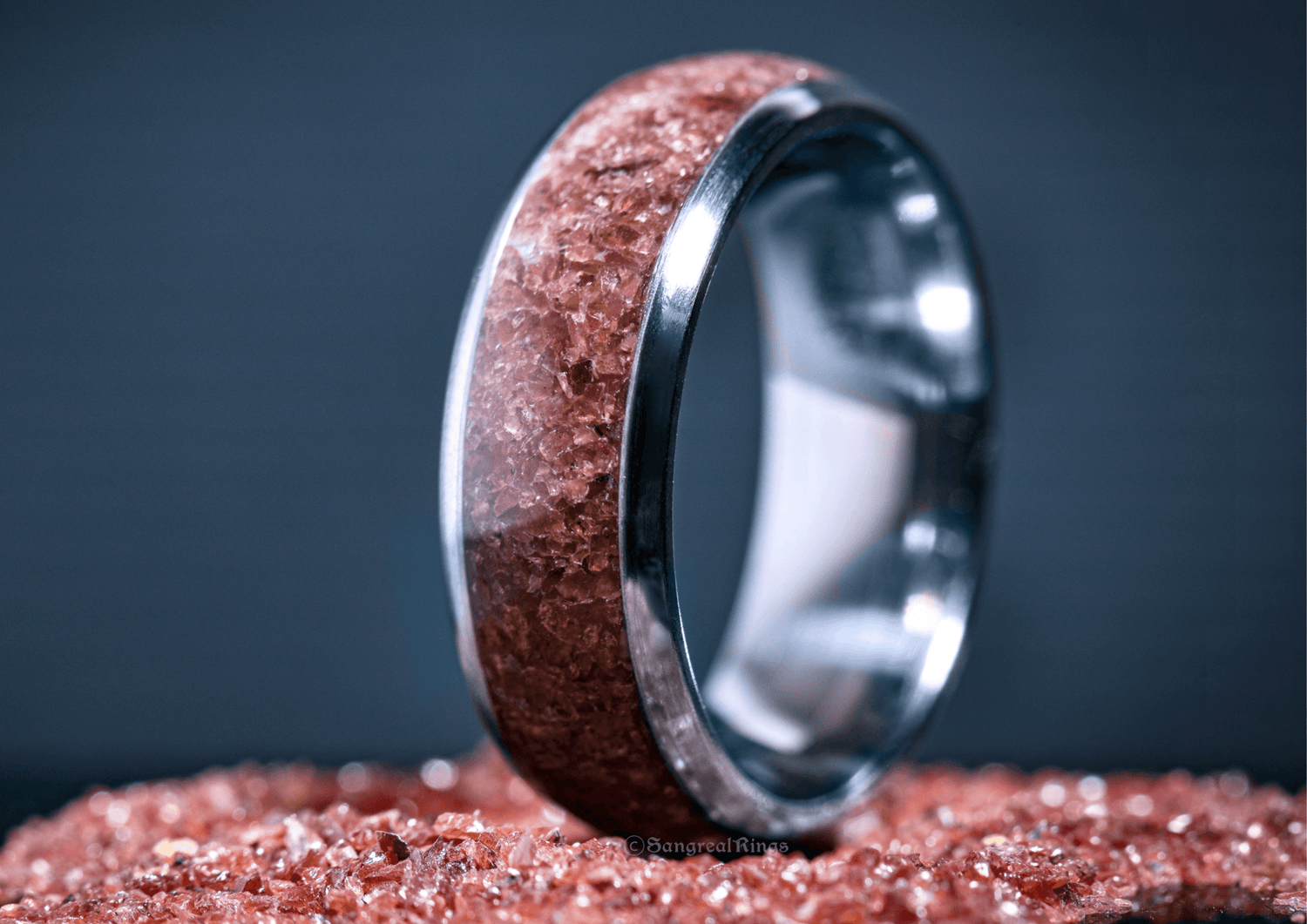 Custom garnet titanium ring with reddish crystal inlay on a dark background