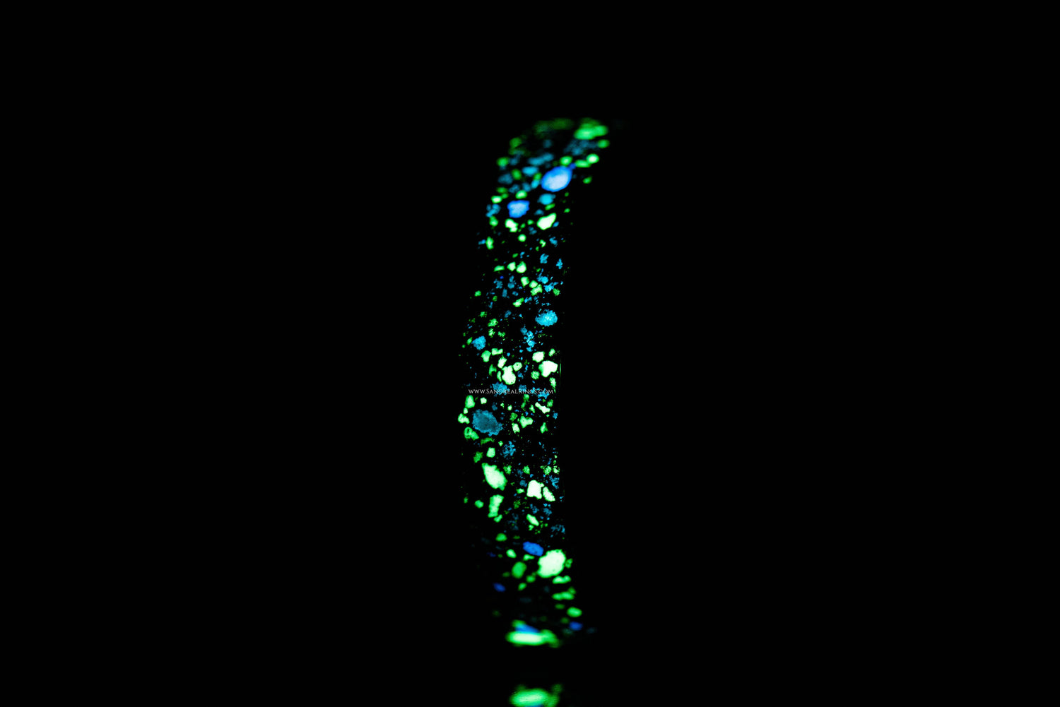 Custom glow in the dark ring by Sangreal Rings glowing with blue and green lights in darkness