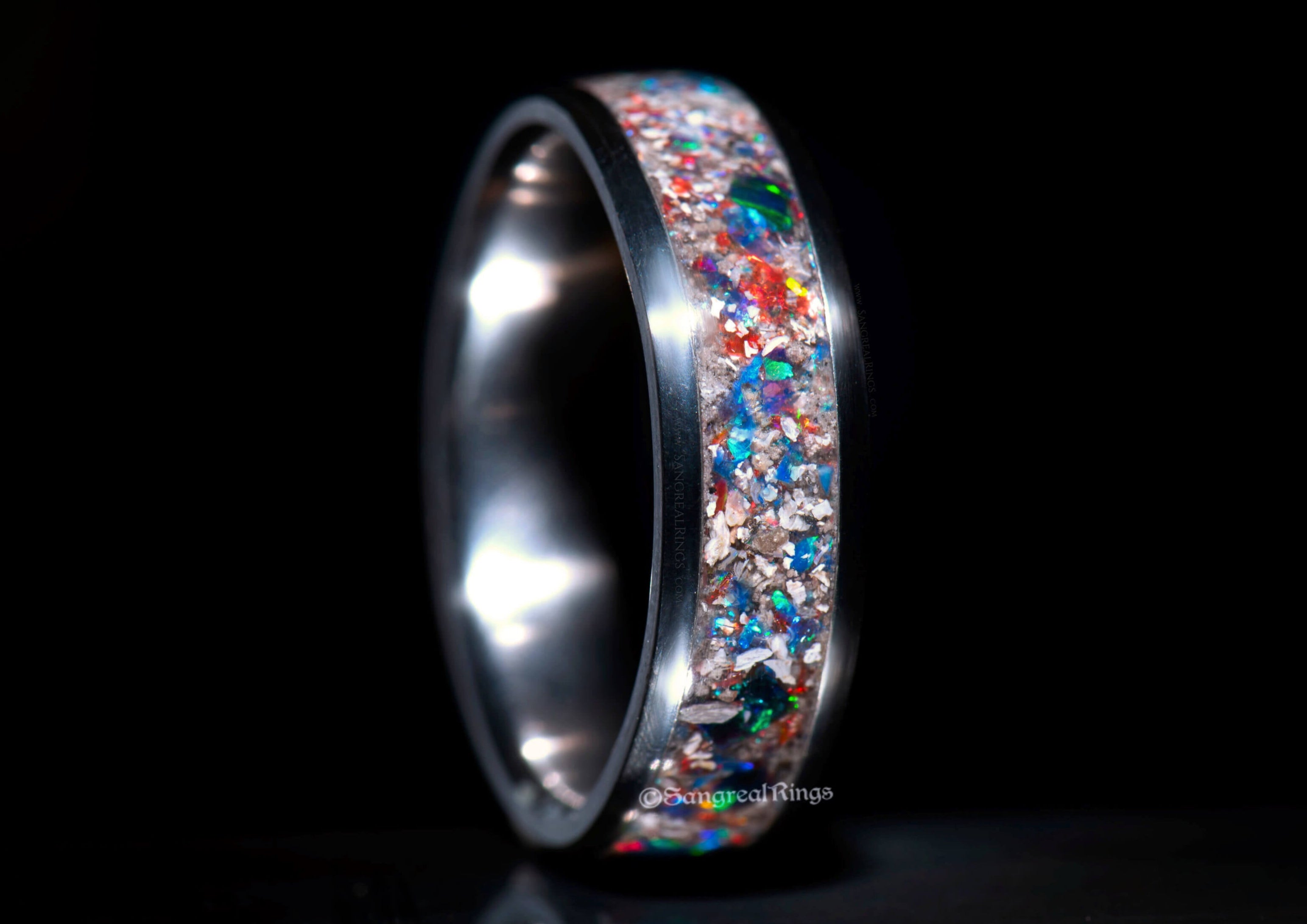 Titanium memorial ring with embedded cremation ashes and colorful opal on a dark baxkground, a unisex keepsake band handcrafted in the UK by SangrealRings.