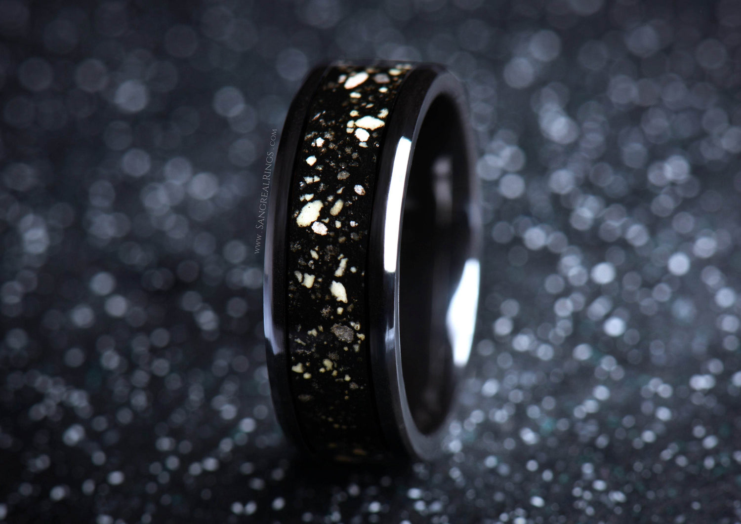 Sleek black ceramic sand ring with gold flecks on a textured dark background