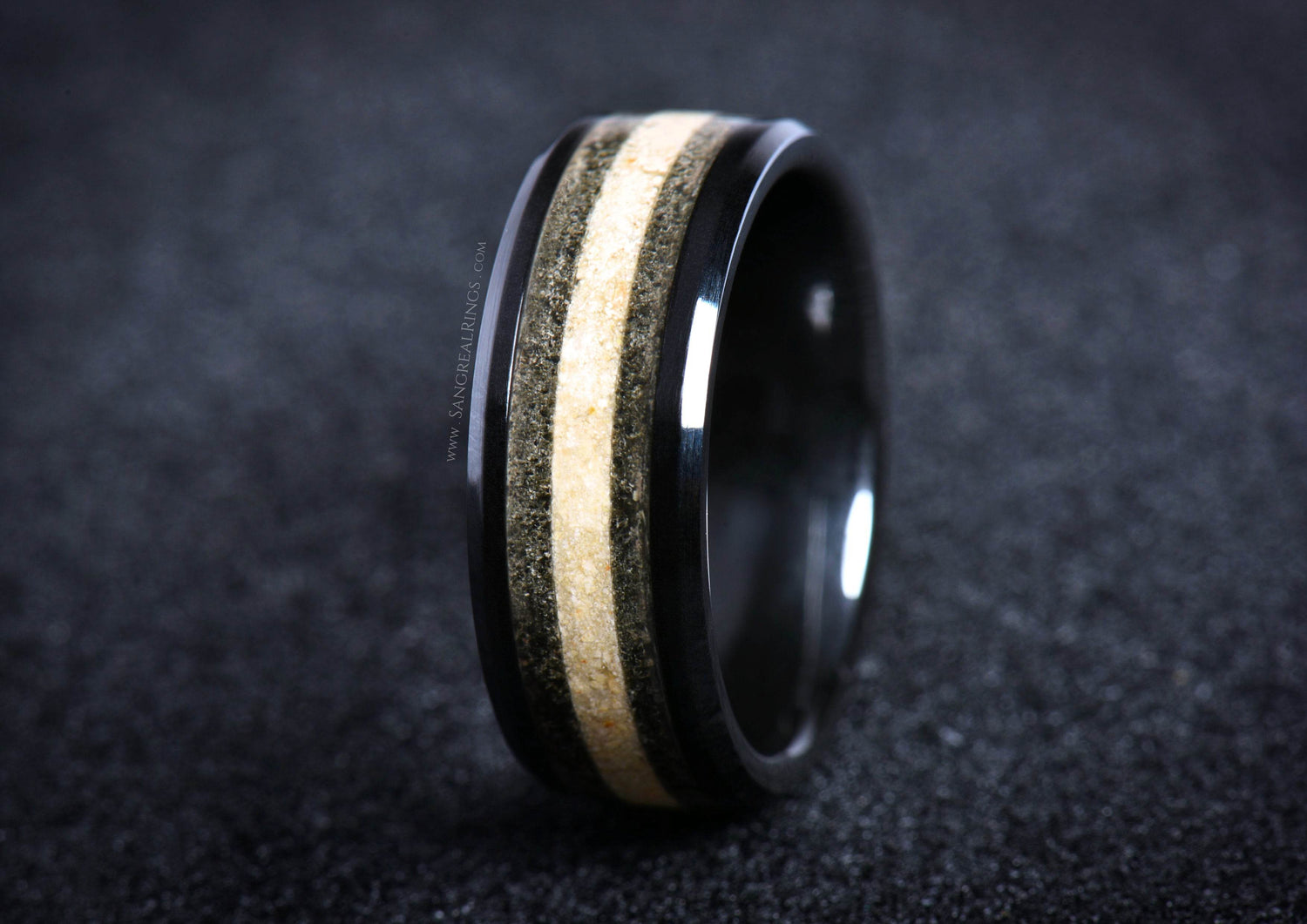 Black ceramic sand ring with contrasting light and dark sand inlay bands on dark background