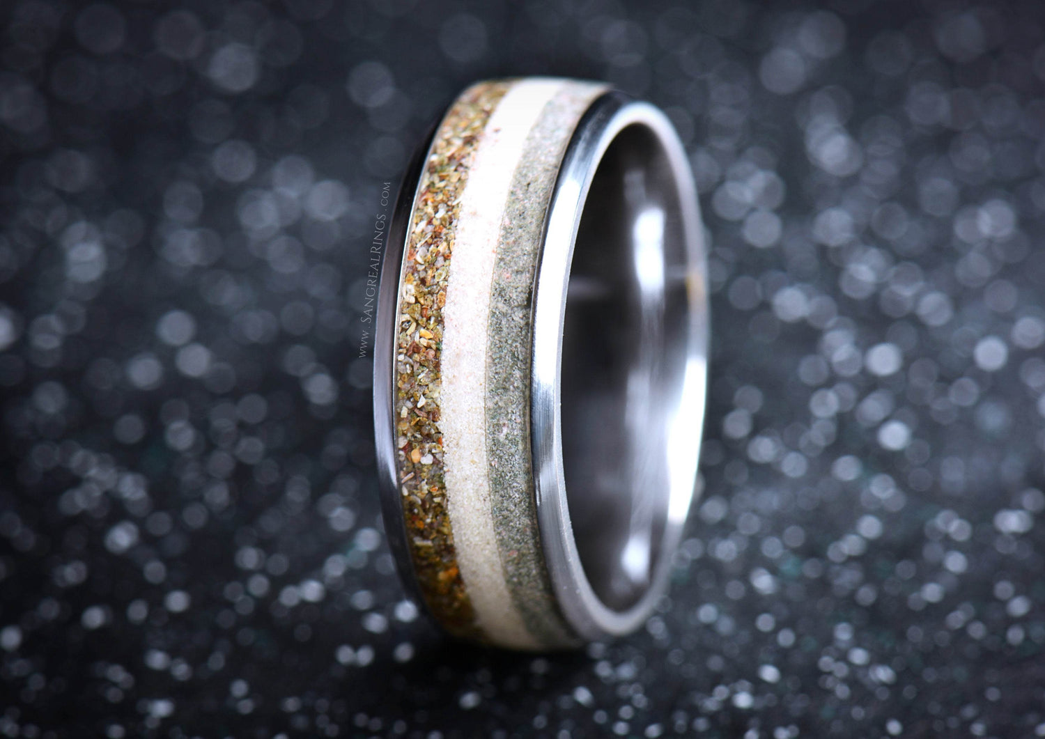 Close-up of a titanium sand ring by Sangreal Rings with layers of sand and metal against a dark background