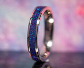 Close-up of a purple opal titanium ring with vibrant blue and purple inlay on a reflective surface