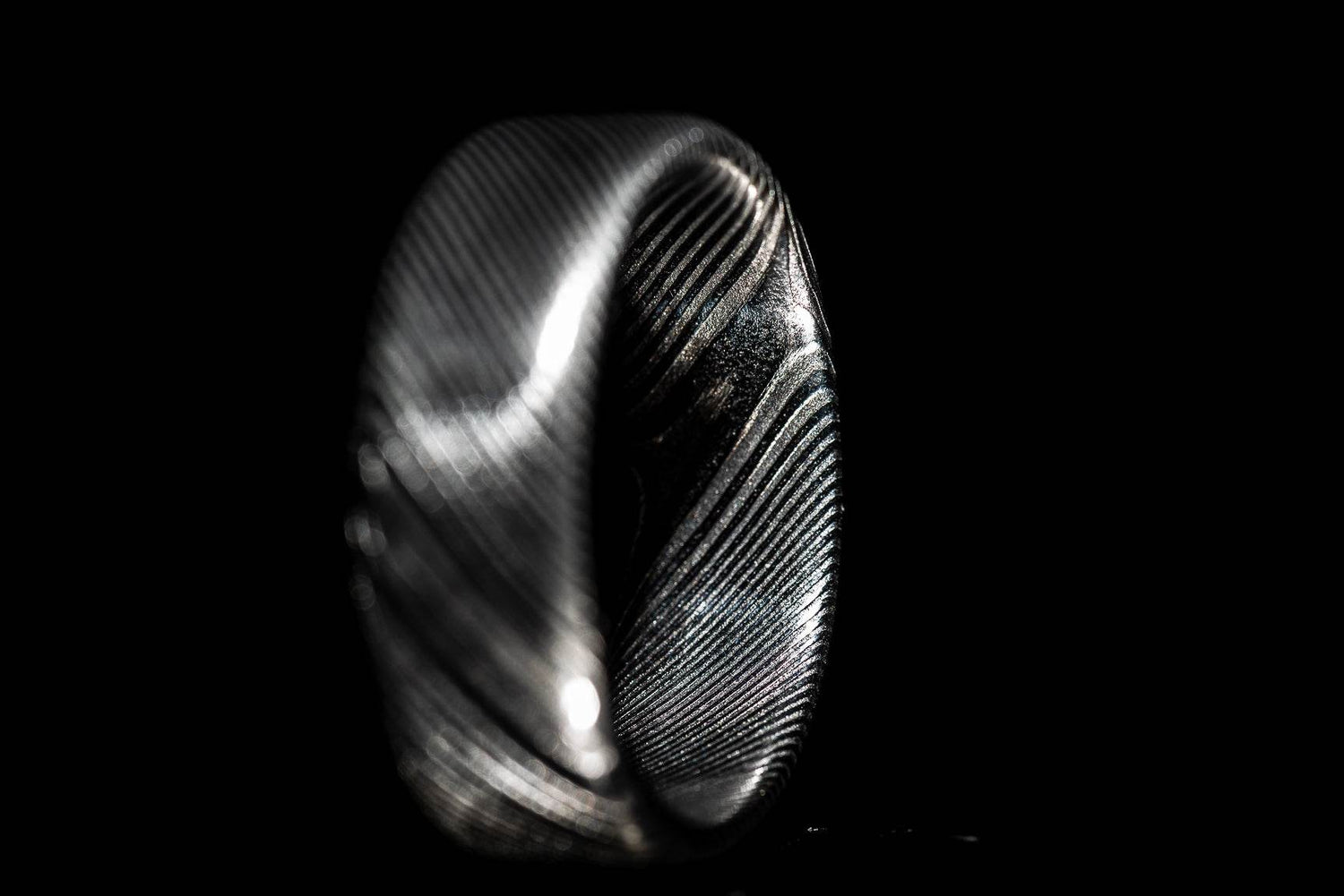Handmade Damascus steel ring with intricate textured pattern on black background by Sangrealrings