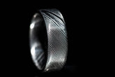 Close-up of a handmade Damascus steel ring with intricate patterned design on a black background