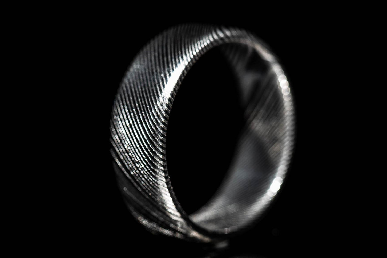 Close-up of a handmade Damascus steel ring with intricate wave pattern on black background