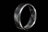 Close-up of a handmade Damascus steel ring with intricate wave pattern on black background