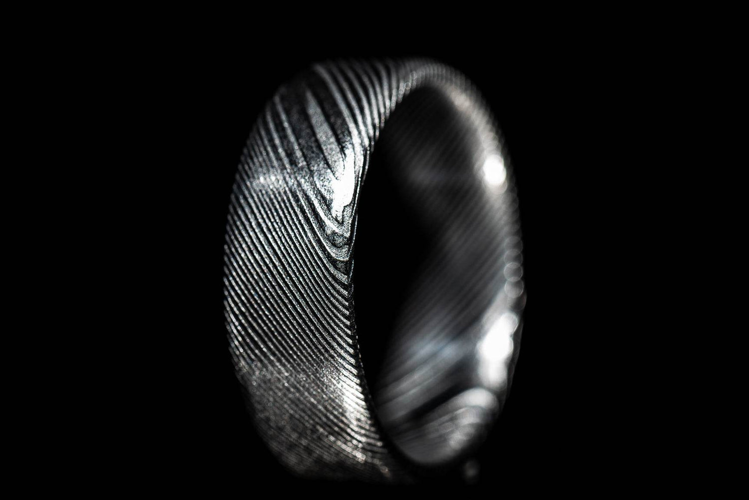 Close-up of a handmade Damascus steel ring with intricate layered patterns on black background
