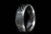 Close-up of a handmade Damascus steel ring with intricate layered patterns on black background