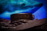 Opal megalodon tooth meteorite ring with dark stone texture displayed on rock with a shark background