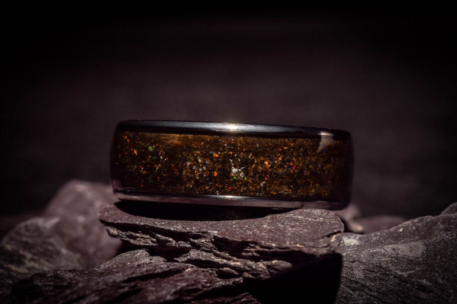 Opal megalodon tooth meteorite ring with glittering inlay resting on dark textured stones