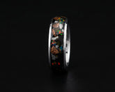 A polished silver-toned ring featuring a black inlay filled with colorful opal-like mineral fragments, shown against a dark black background.
