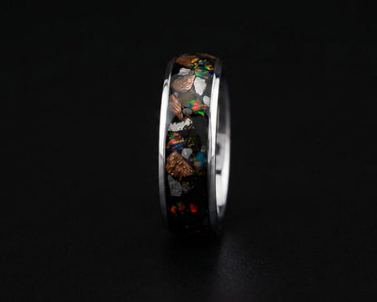 A polished silver-toned ring featuring a black inlay filled with colorful opal-like mineral fragments, shown against a dark black background.