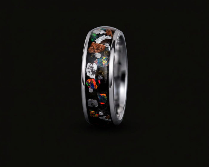 A polished silver-toned ring featuring a black inlay filled with colorful opal-like mineral fragments, shown against a solid black background.
