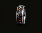 A polished silver-toned ring featuring a black inlay filled with colorful opal-like mineral fragments, shown against a solid black background.