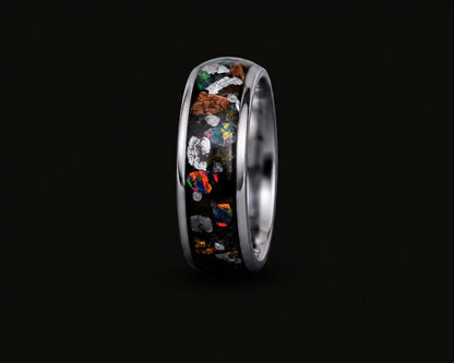 A polished silver-toned ring featuring a black inlay filled with colorful opal-like mineral fragments, shown against a solid black background.