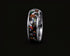 A polished silver-toned ring featuring a black inlay filled with colorful opal-like mineral fragments, shown against a solid black background.