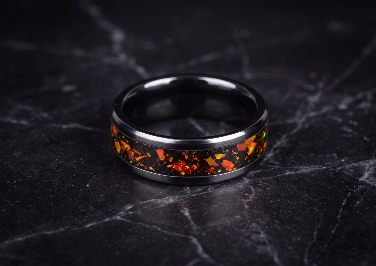 A black ceramic ring band featuring a vibrant orange and red terrazzo inlay, displayed on a dark gray marble surface.