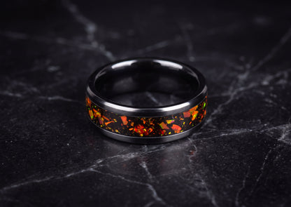 A black ceramic ring band featuring a vibrant orange and red terrazzo inlay, displayed on a dark gray marble surface.