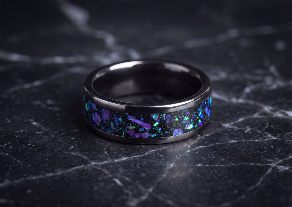 A black ceramicring band featuring a vibrant iridescent inlay of purple, blue, and green opal-like flakes, photographed on a dark marble surface.