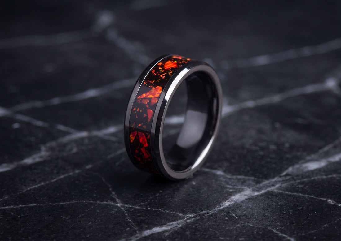 A black ceramic ring with a vibrant red and orange fiery inlay, displayed on a dark marble surface.