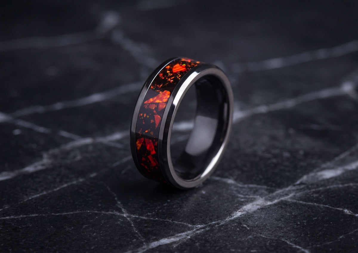 A black ceramic ring with a vibrant red and orange fiery inlay, displayed on a dark marble surface.
