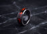 A black ceramic ring with a vibrant red and orange fiery inlay, displayed on a dark marble surface.