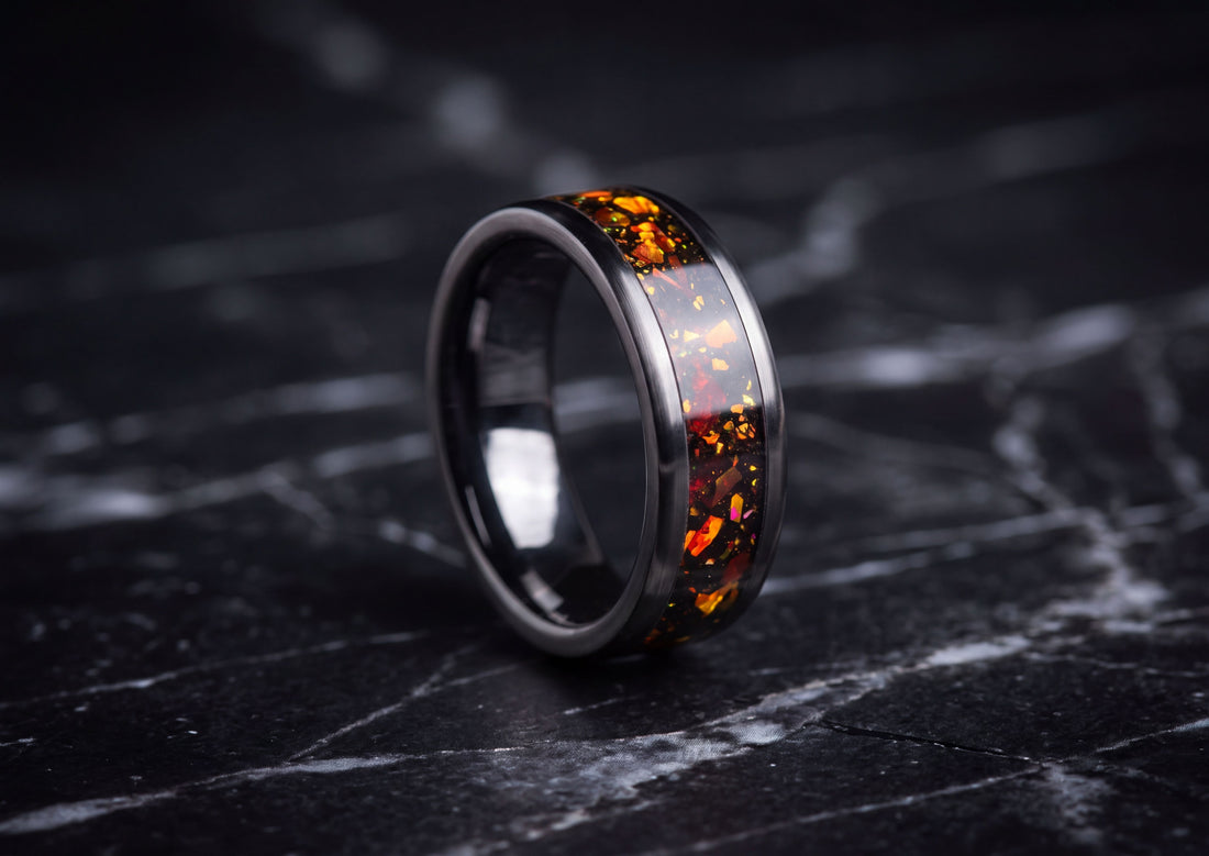 A polished dark ceramic ring with an inlay of orange and yellow fiery flecks on a black marble surface.