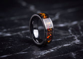 A polished dark ceramic ring with an inlay of orange and yellow fiery flecks on a black marble surface.