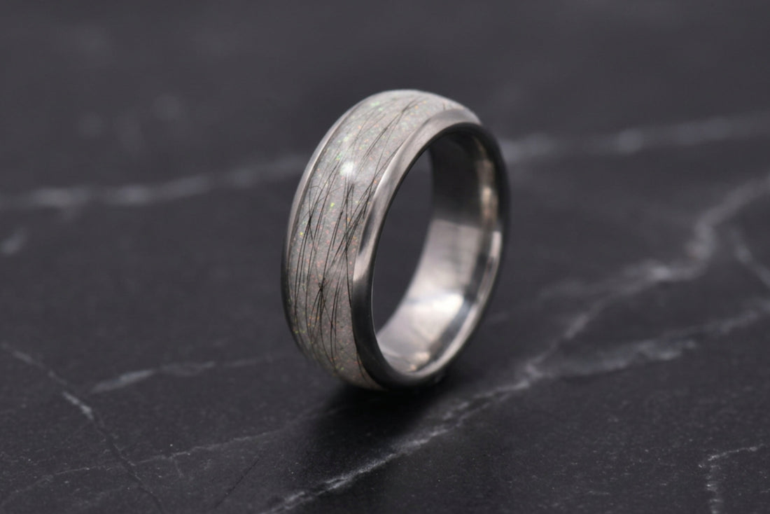 A silver-toned ring with a textured, pet furnlay, standing upright on a dark gray marble surface.
