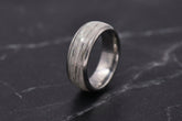 A silver-toned ring with a textured, pet furnlay, standing upright on a dark gray marble surface.
