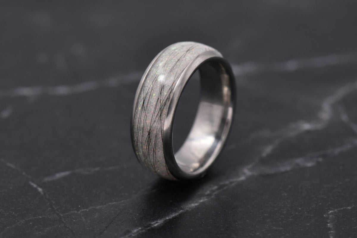 A silver-toned ring with a textured, pet furnlay, standing upright on a dark gray marble surface.