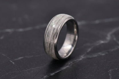 A silver-toned ring with a textured, pet furnlay, standing upright on a dark gray marble surface.
