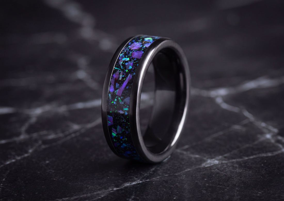 A black ceramic ring with a vibrant purple and blue opal inlay, displayed on a dark marble surface.