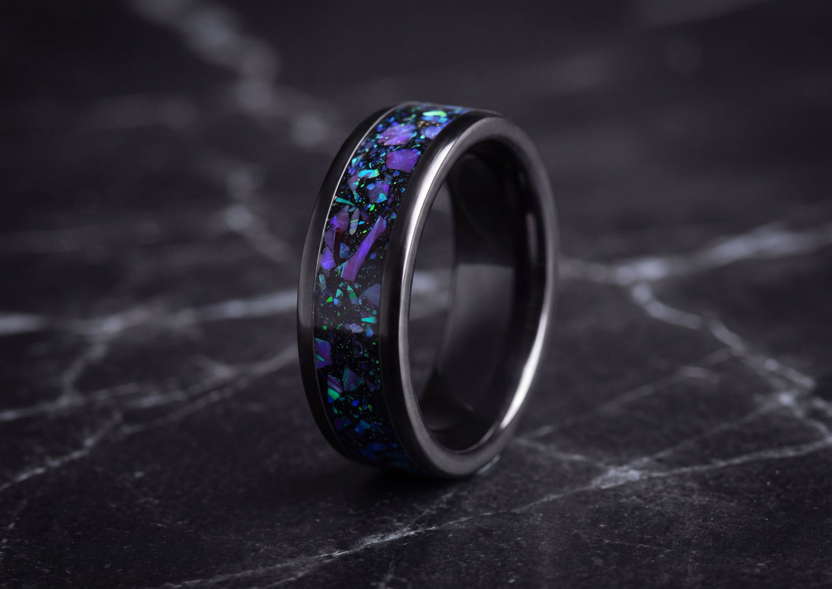 A black ceramic ring with a vibrant purple and blue opal inlay, displayed on a dark marble surface.