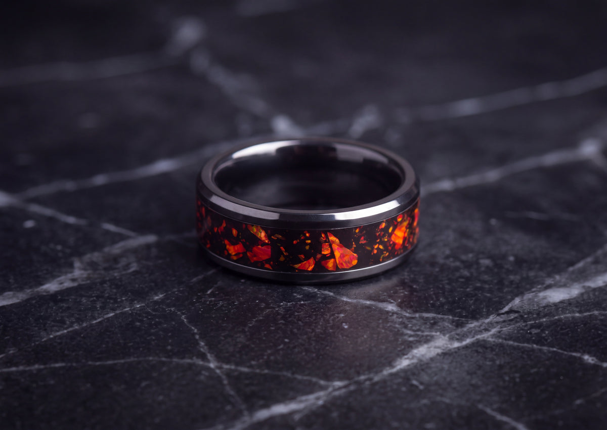 A black ceramic ring band featuring a vibrant orange and red fiery inlay, resting on a dark gray marble surface.