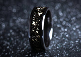 Sleek black ceramic sand ring with gold flecks on a textured dark background