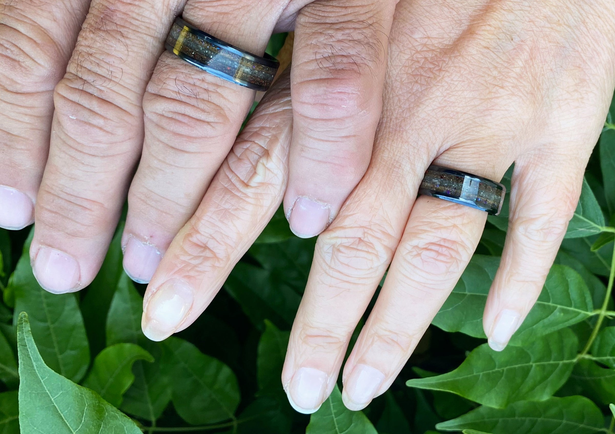 Two hands with wedding rings on a green leafy background