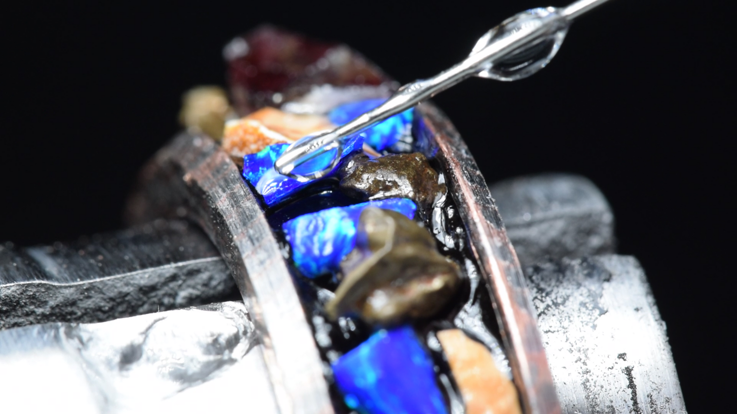 Close-up of a jewelry-making process with a ring featuring blue stone and gold accents.